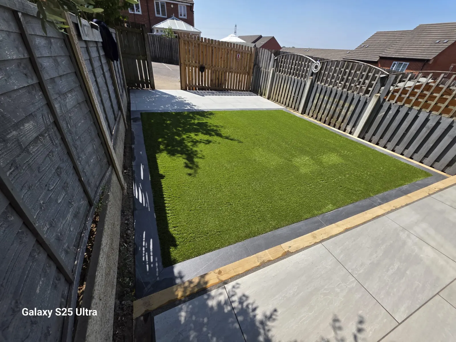 Artificial grass lawn with a sleeper edge beside a porcelain patio