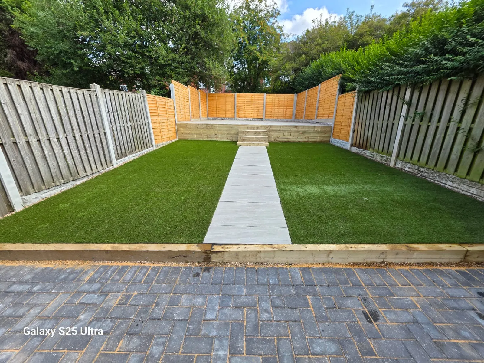 Artificial grass either side of a porcelain path up to a raised sleeper deck