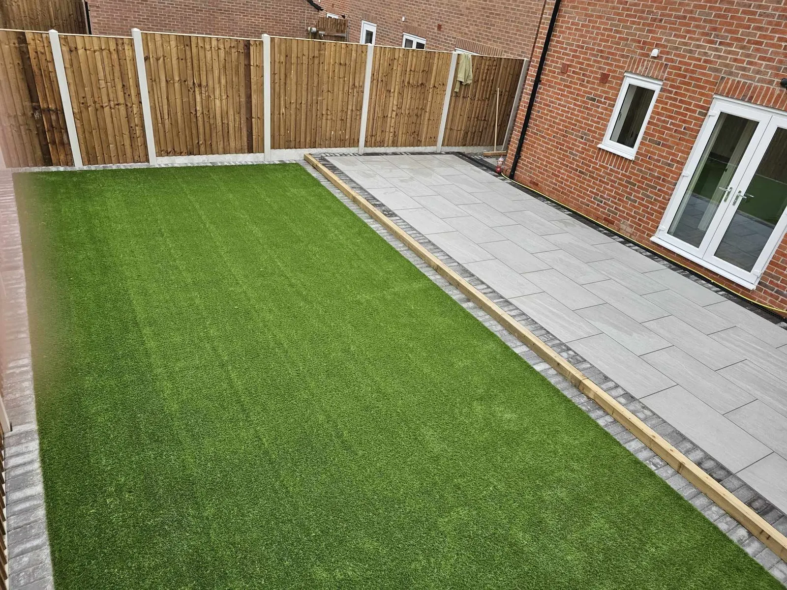 Artificial grass beside a porcelain path with a sleeper edge
