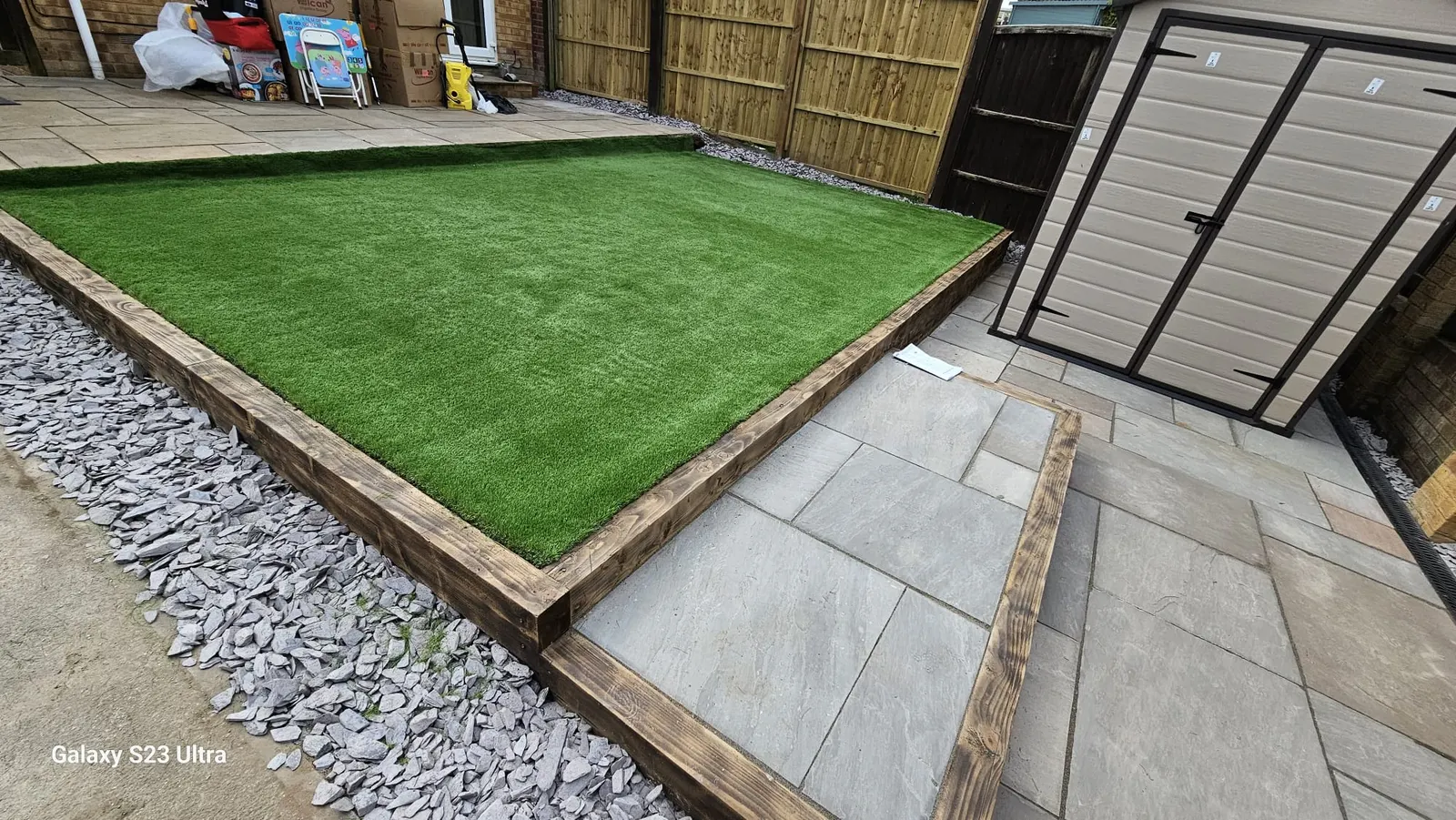 Artificial grass in a sleeper frame with a porcelain path and gravel