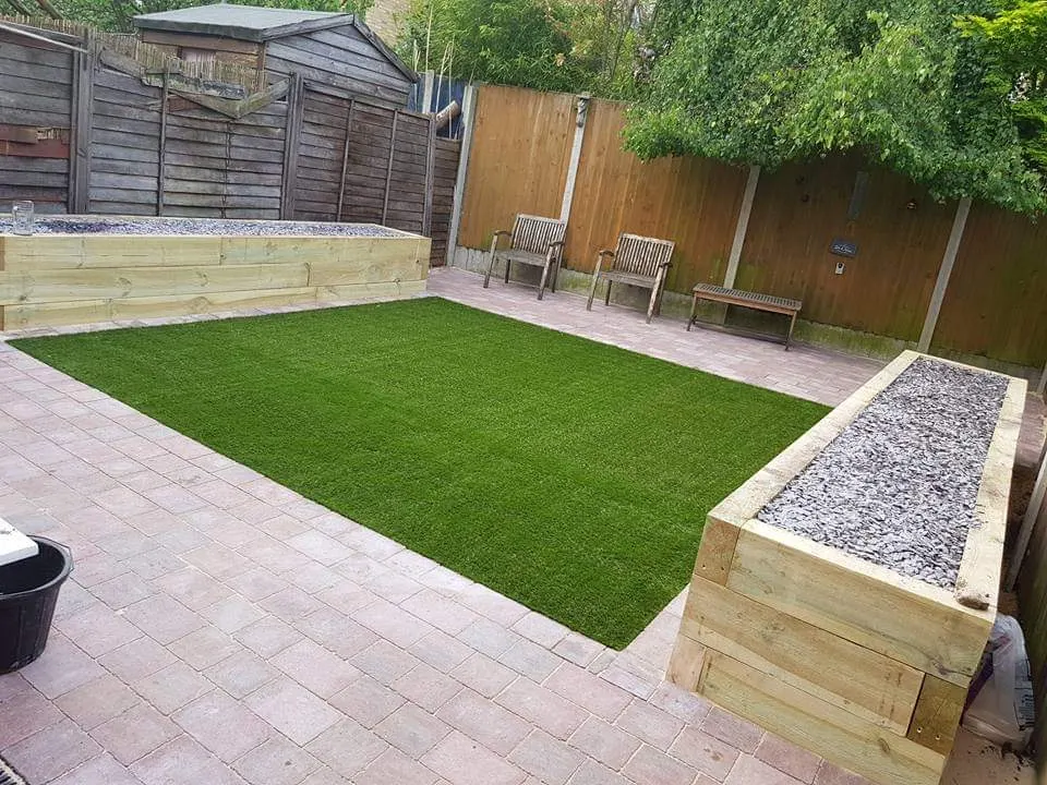 Artificial grass framed by sleeper raised beds and a paved edge