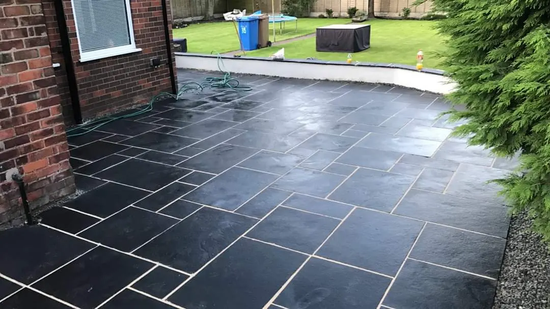 Black slate patio below a rendered wall and a raised lawn