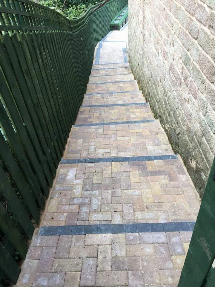 Block paving steps up a narrow passage between a stone wall and a fence