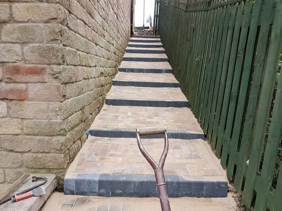 Block paving steps with charcoal nosings being laid in a narrow side passage