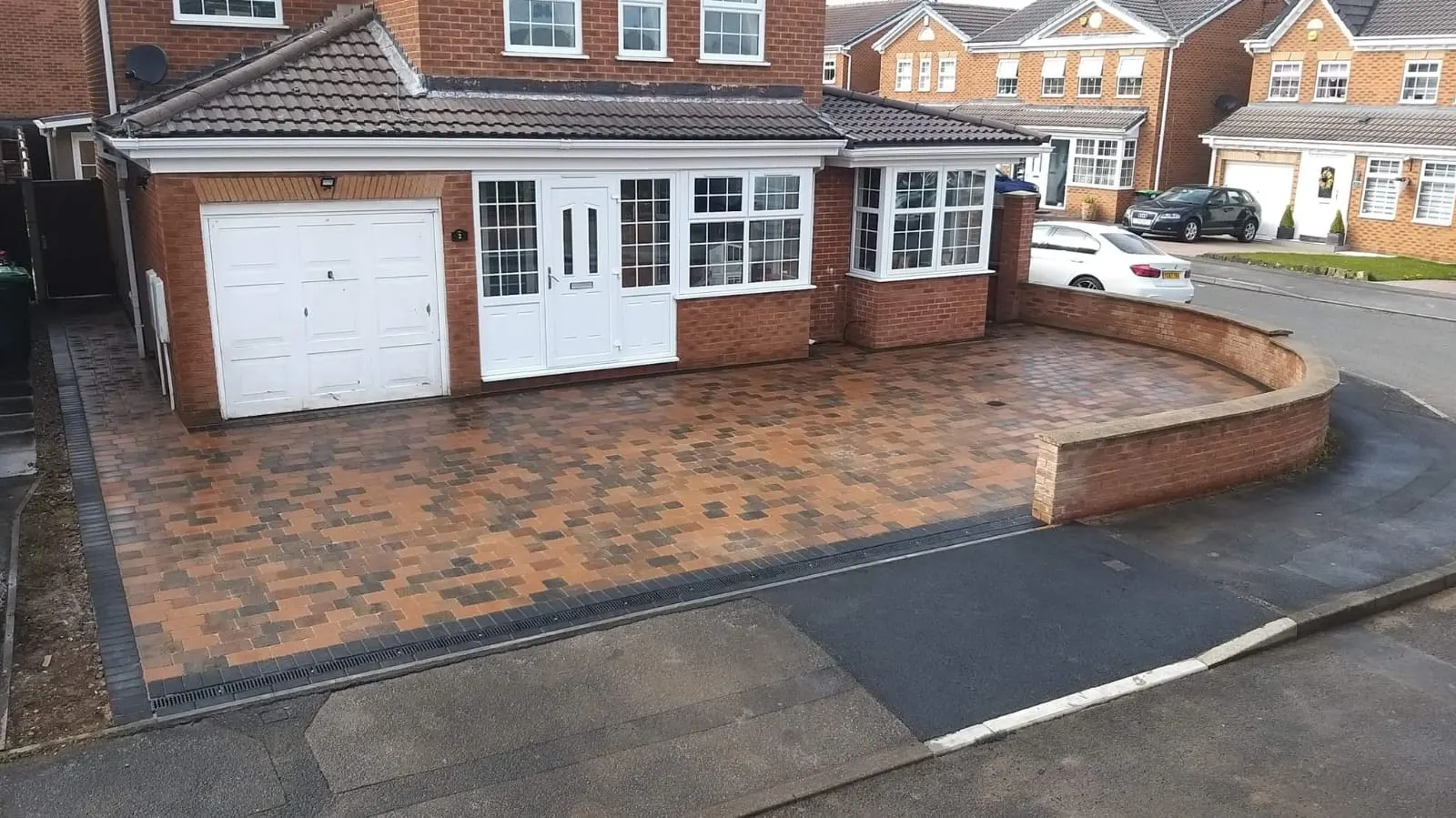 Brindle cobble-effect block paving driveway with a curved brick wall