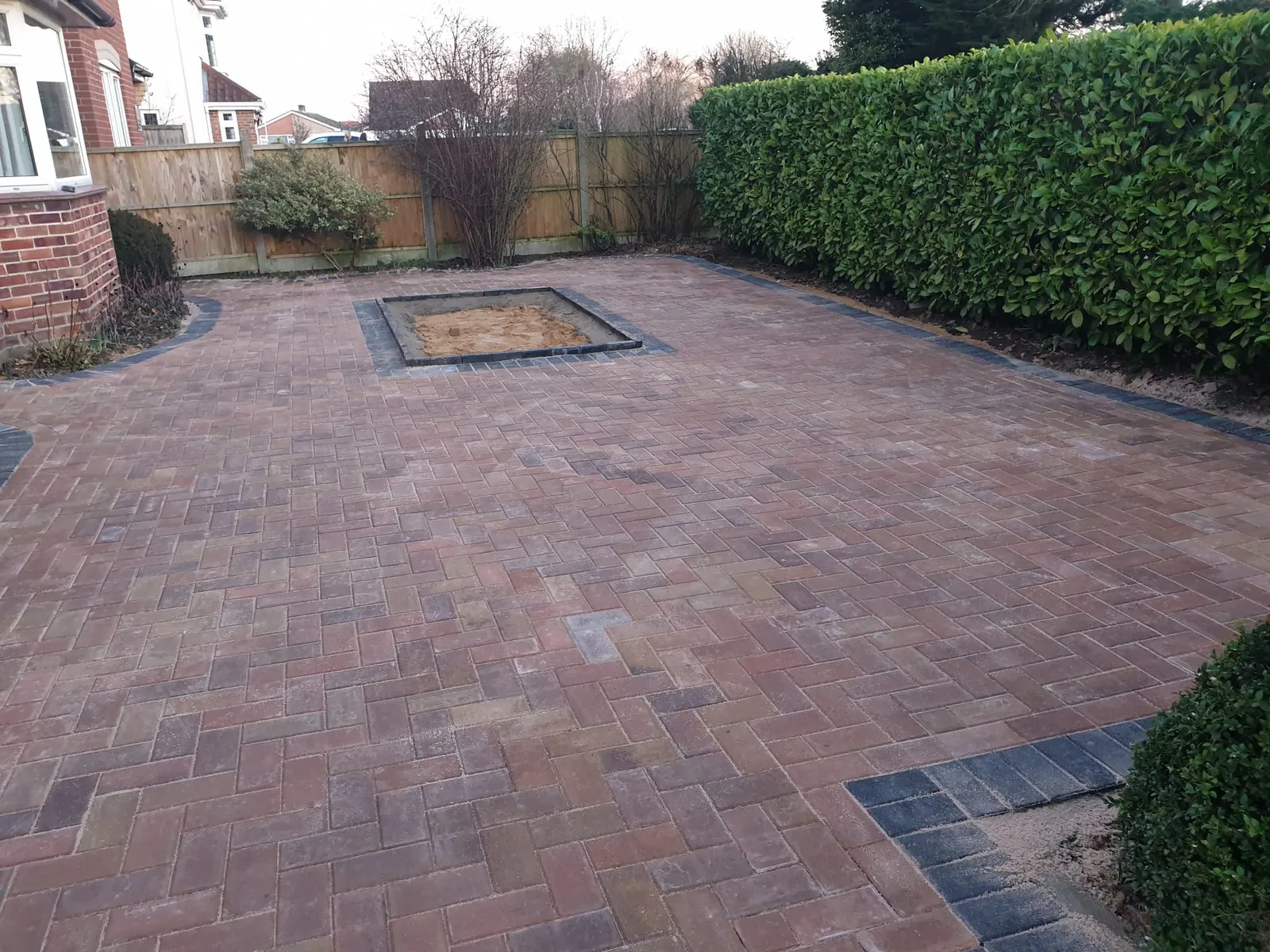 Brindle block paving driveway with a square planting bed and a hedge