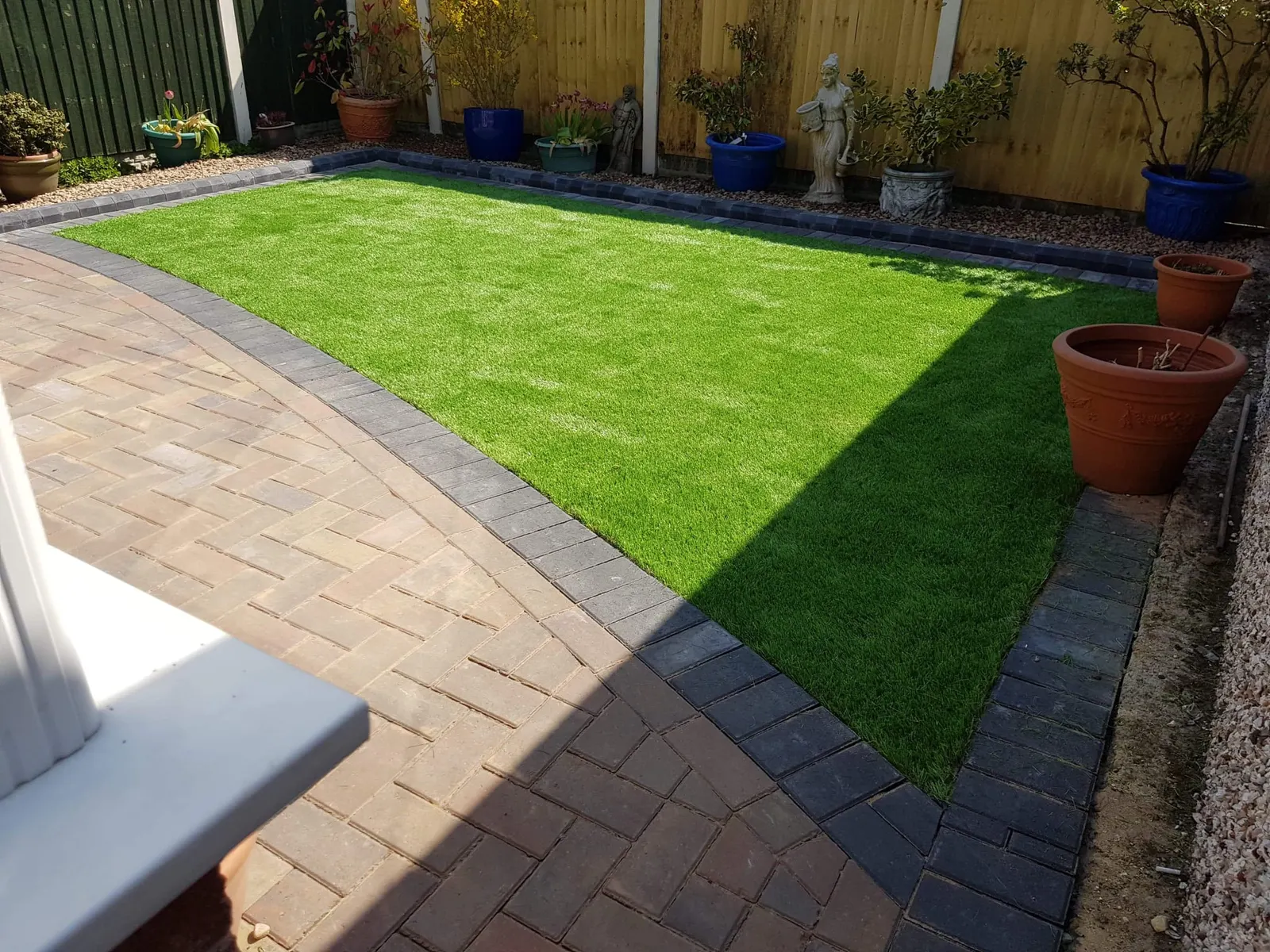 Brindle block paving path and lawn in a front garden with potted plants