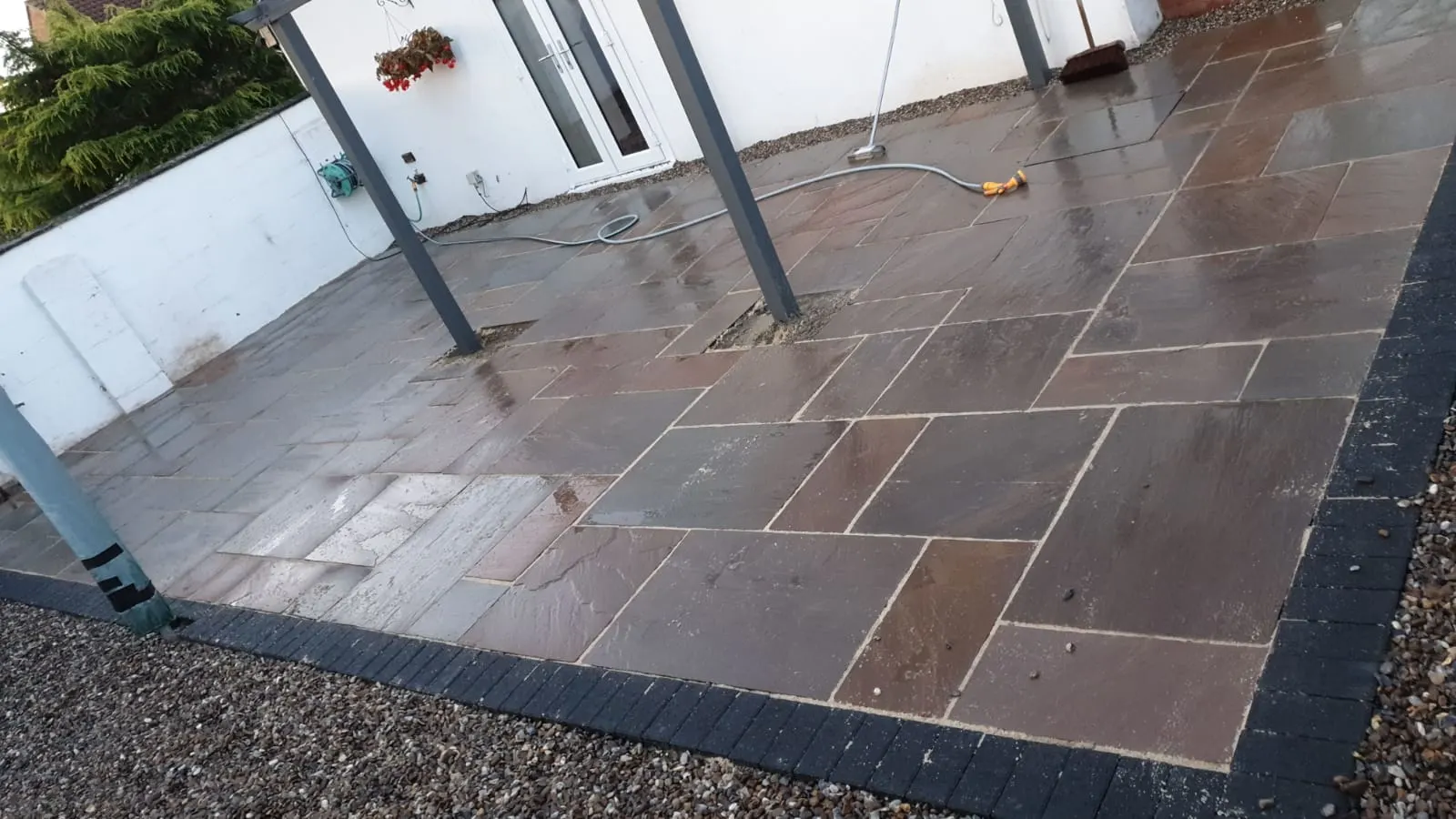 Brown Indian sandstone patio with a charcoal border under a pergola