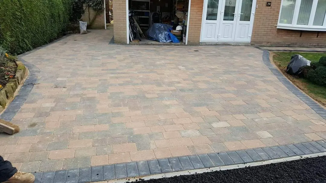 Buff block paving driveway with a charcoal border in front of a garage