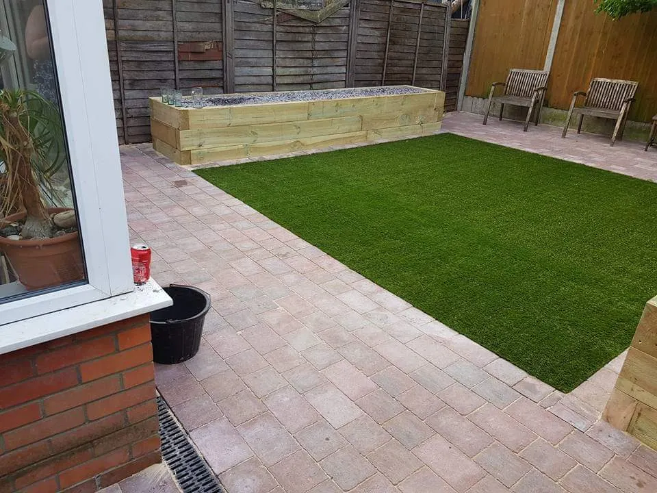 Buff block paving patio around artificial grass with a sleeper raised bed