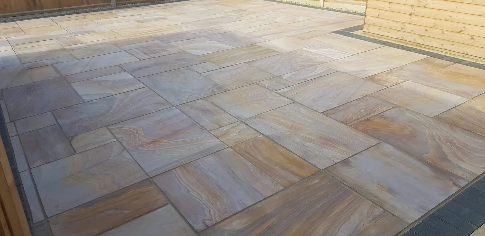 Buff Indian sandstone patio in the corner of a fenced garden
