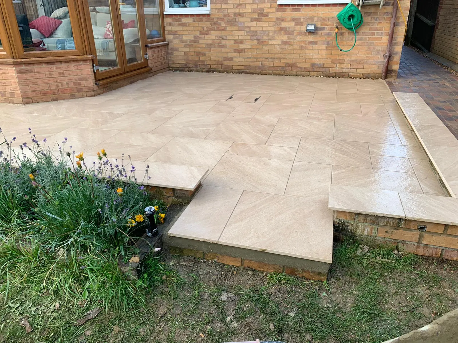 Buff porcelain patio with a step down to the lawn