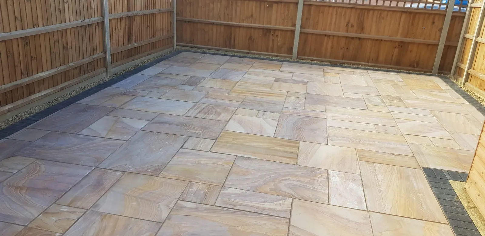 Buff sandstone patio with a charcoal edge in a fenced garden
