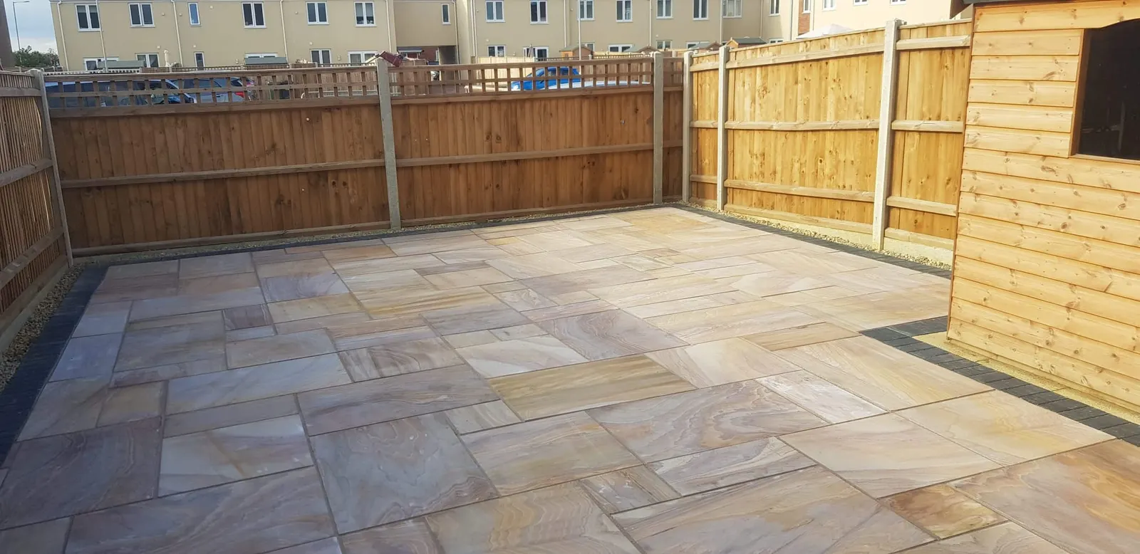 Buff sandstone patio in a fenced garden beside a timber shed
