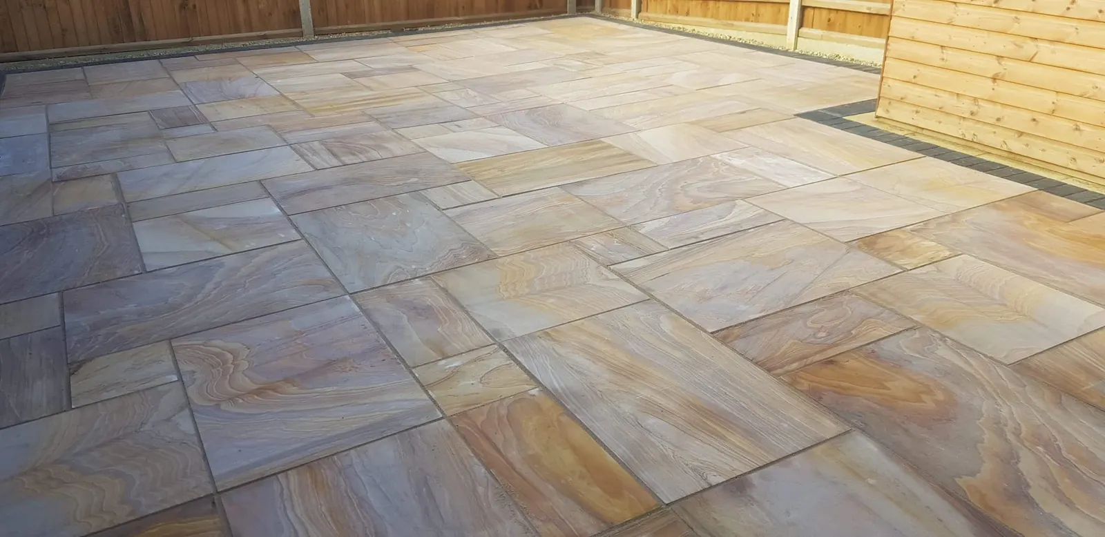 Wide buff sandstone patio filling a fenced garden