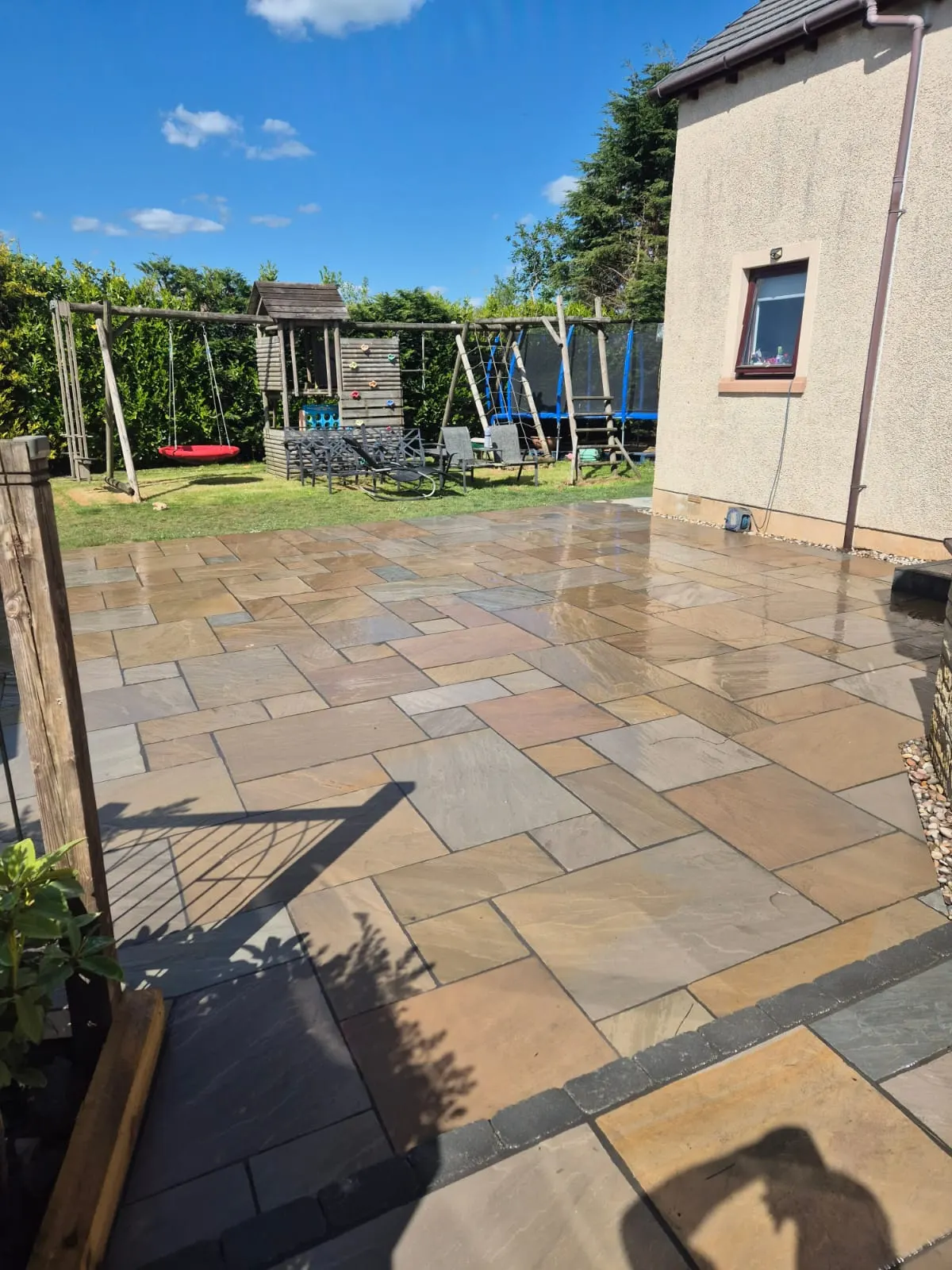 Buff sandstone patio after rain beside a garden play area