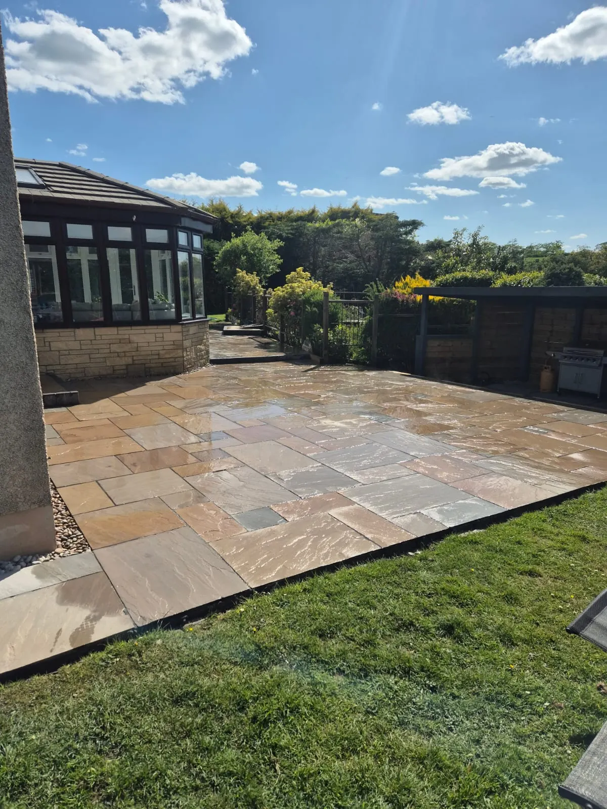 Buff sandstone patio beside a lawn and a conservatory