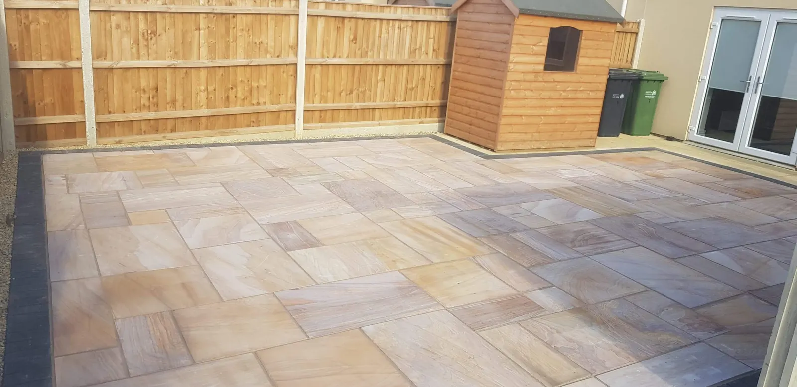 Buff sandstone patio with a shed in a fenced garden
