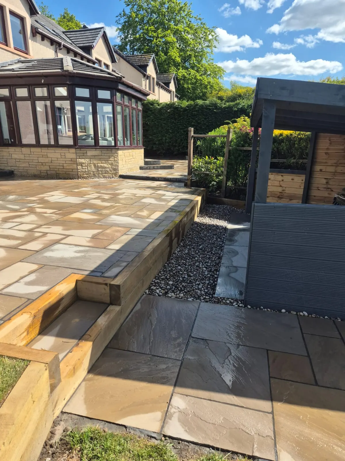 Buff sandstone patio with a sleeper raised bed beside a conservatory