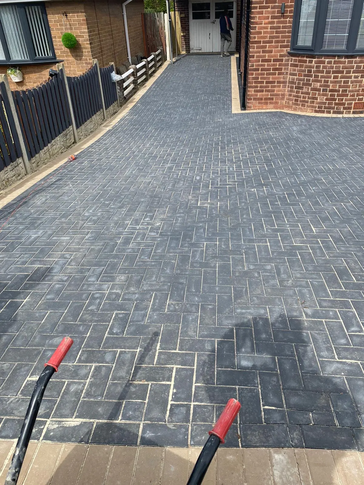 Charcoal herringbone block paving driveway beside railings