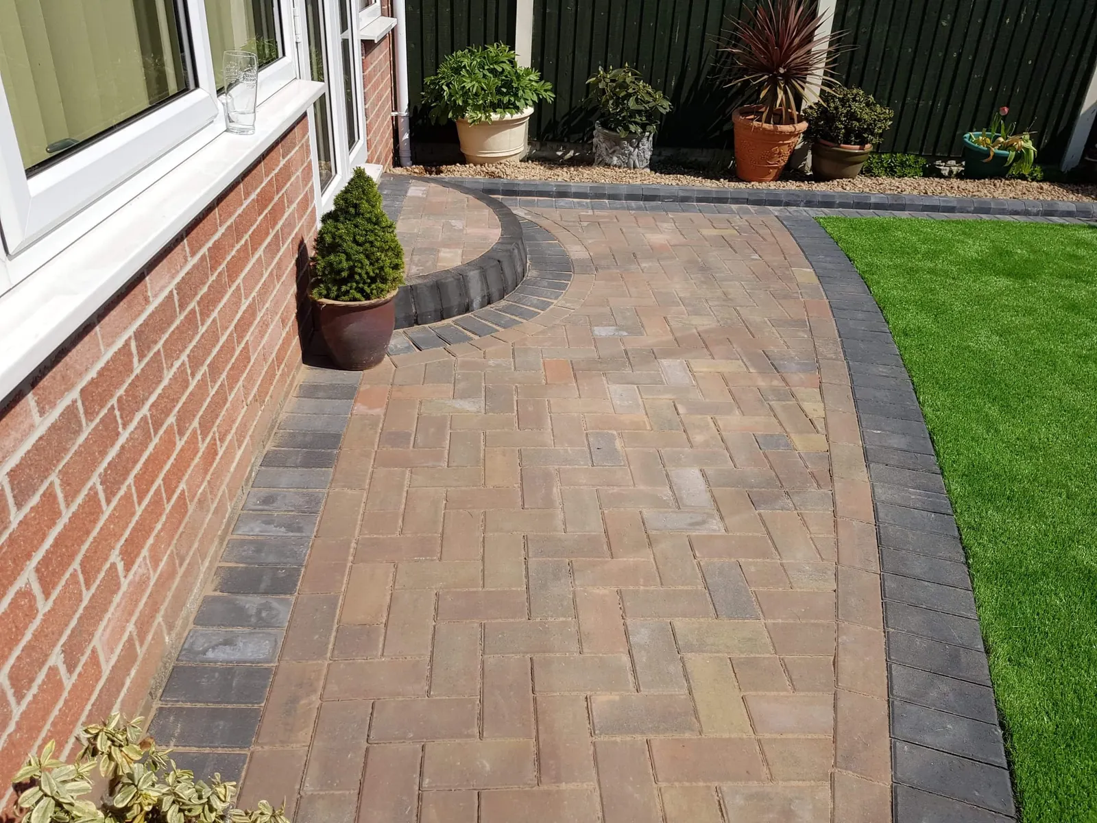 Curved brindle block paving path with a charcoal border beside a lawn