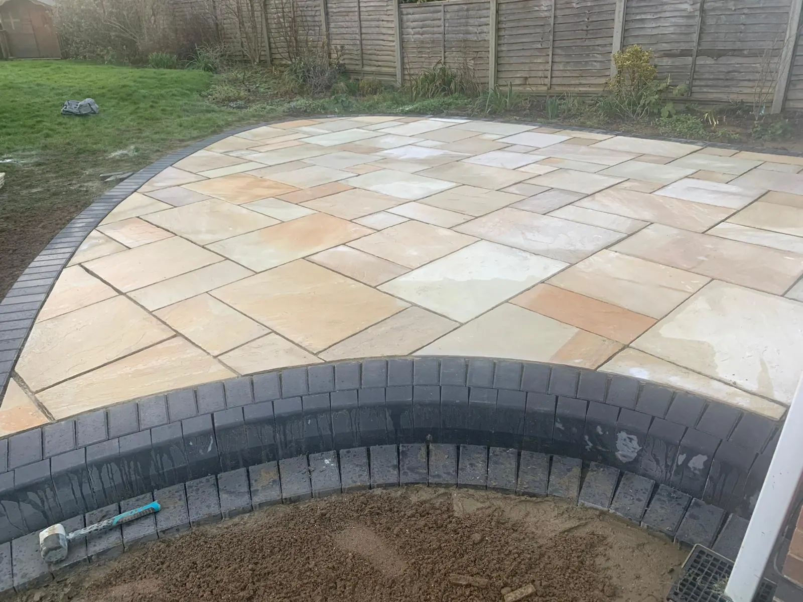 Curved buff sandstone patio with a charcoal block edge