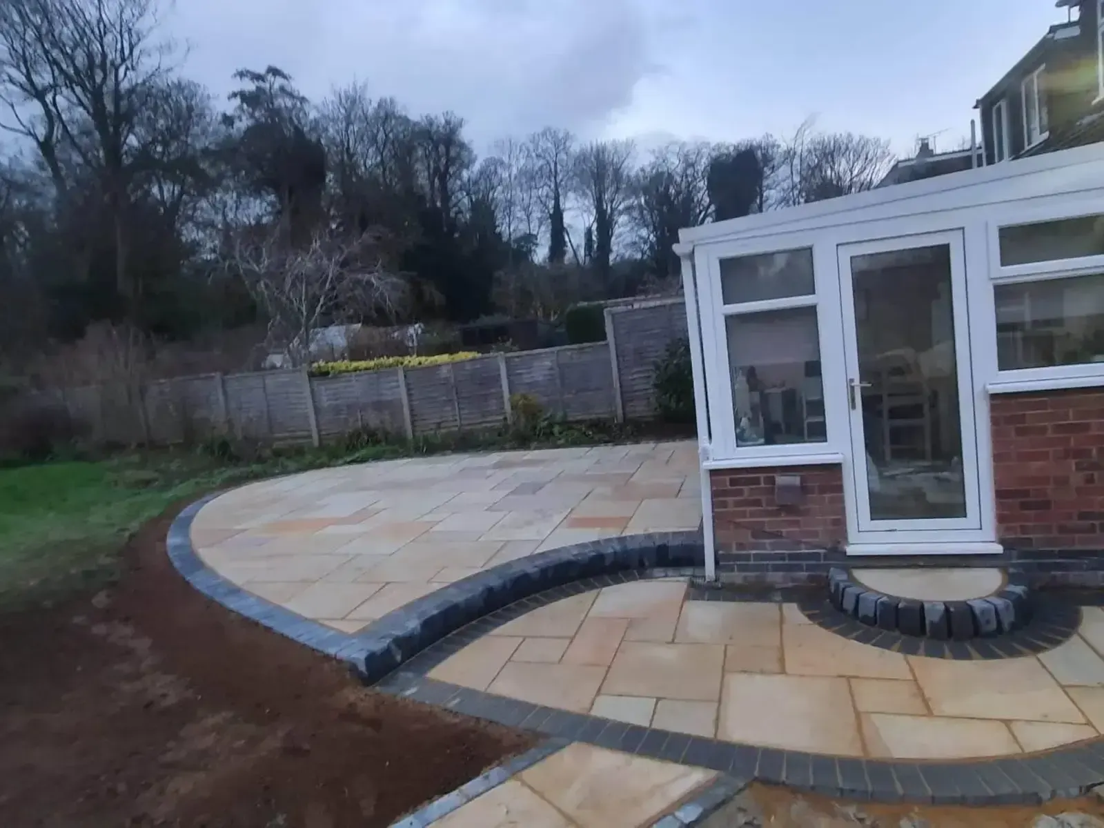 Curved sandstone patio outside a conservatory, edged in block paving