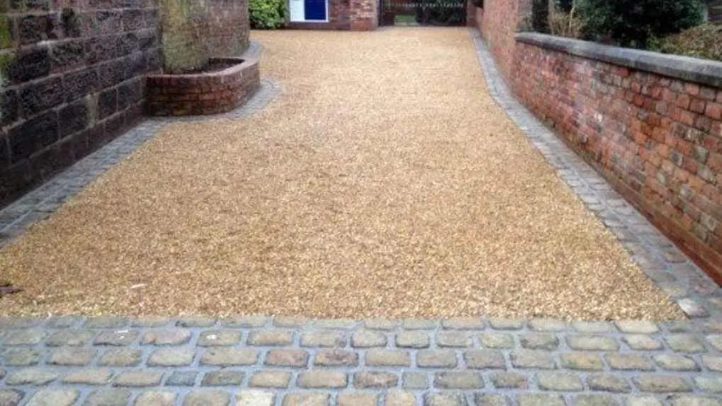 Gravel driveway with cobble block edging between brick walls
