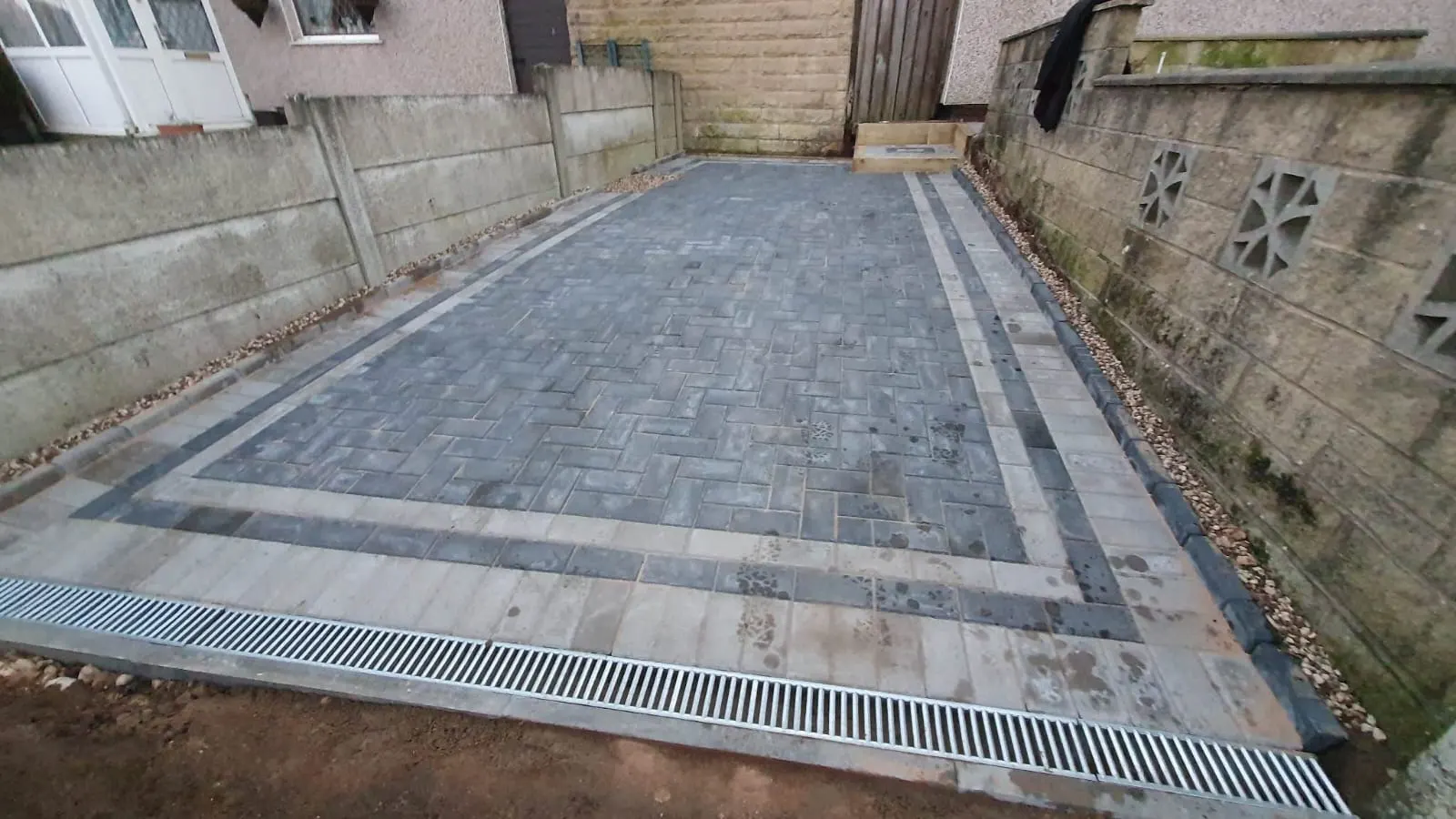 Grey block paving driveway with a light border and a channel drain between walls