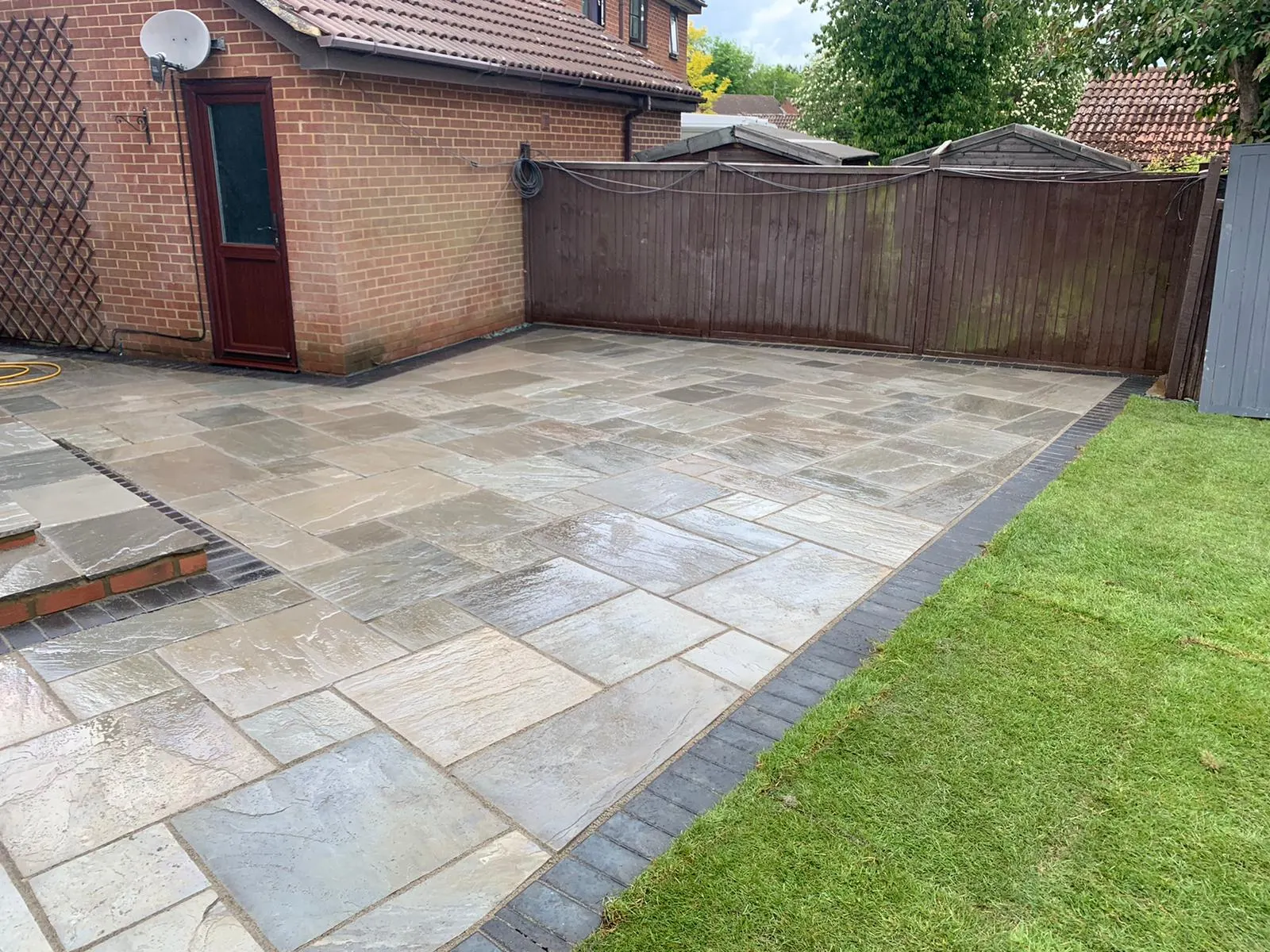 Grey Indian sandstone patio with a charcoal edge beside a new lawn