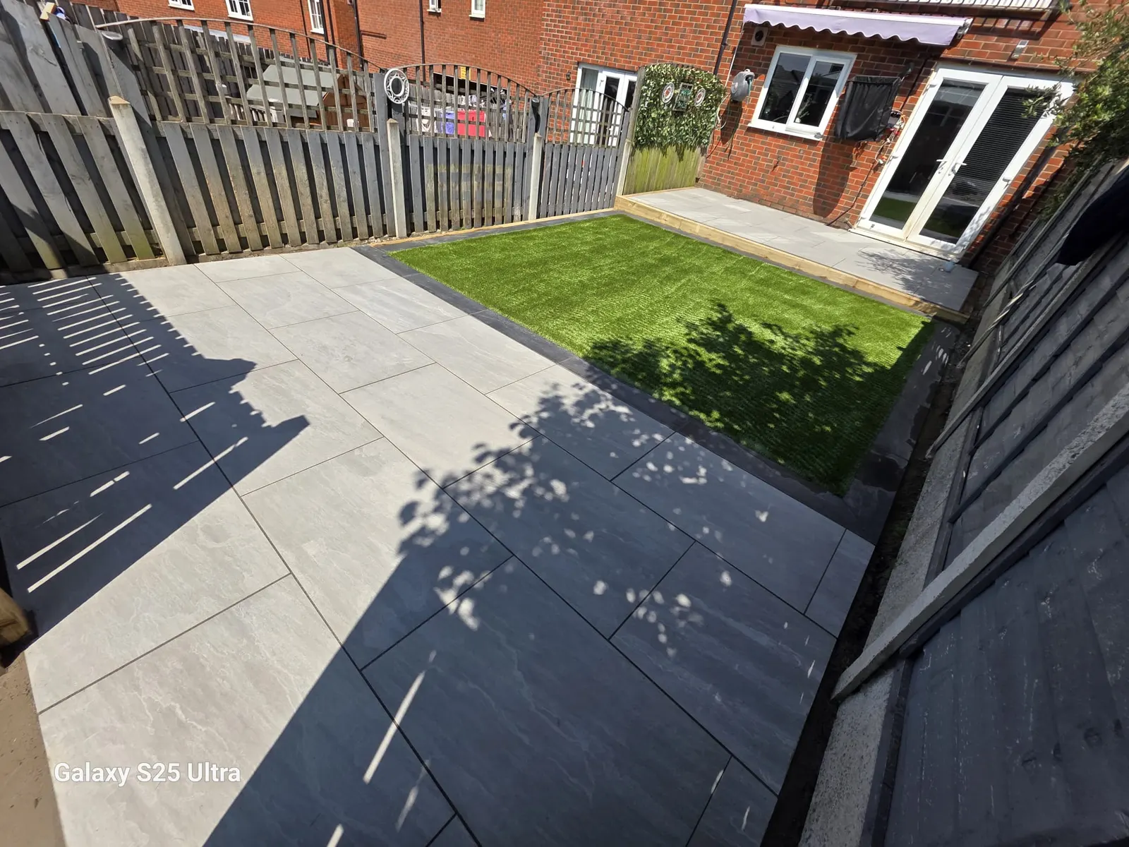 Grey porcelain patio and artificial grass in a fenced garden