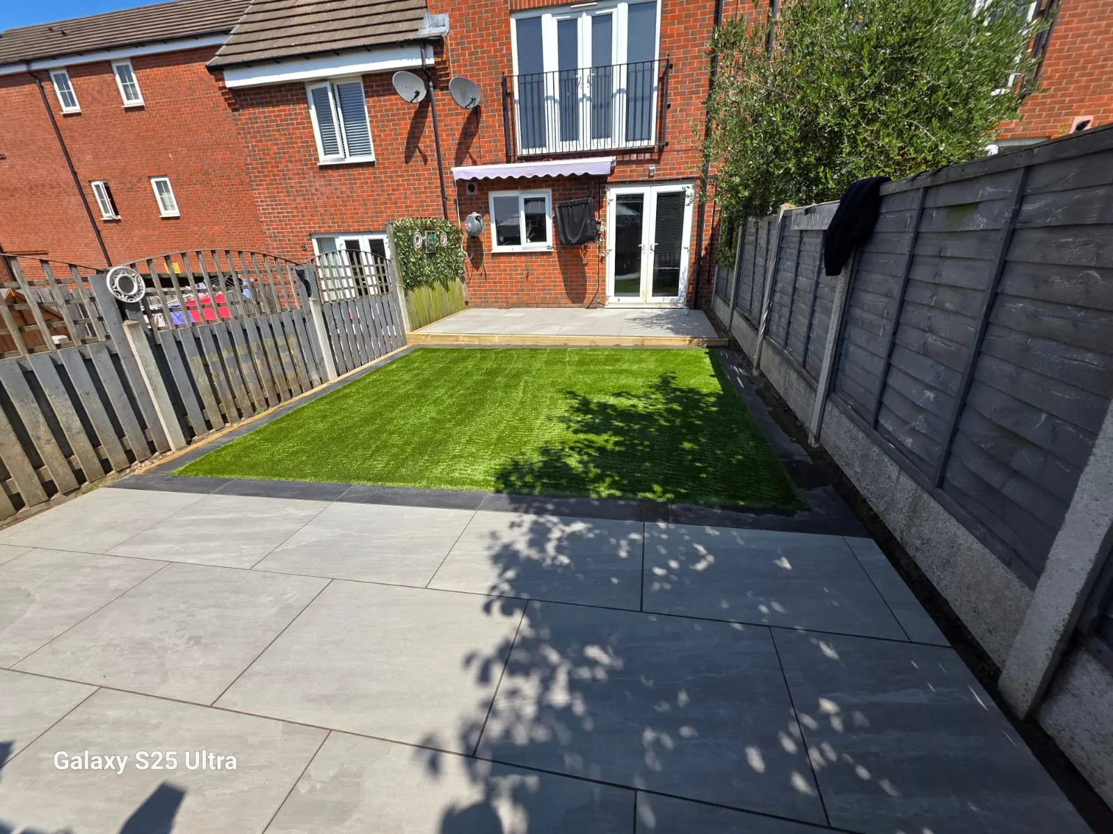 Grey porcelain patio and artificial grass behind a town house