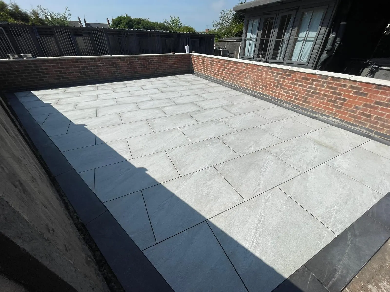 Grey porcelain patio with a charcoal edge between brick walls