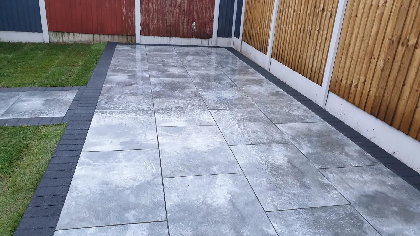 Grey porcelain patio with a charcoal edge between two lawns
