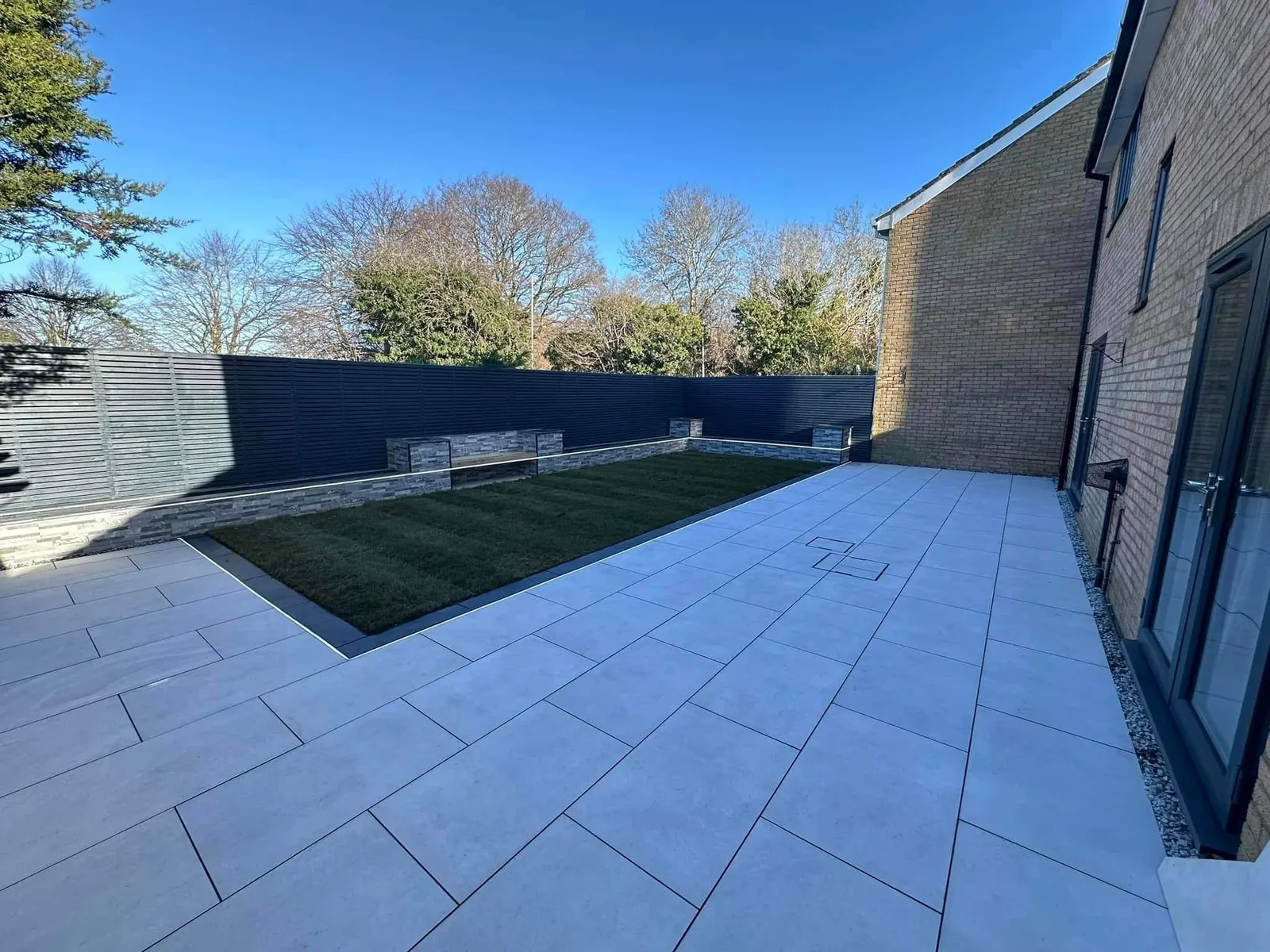 Grey porcelain patio and lawn behind a new-build house