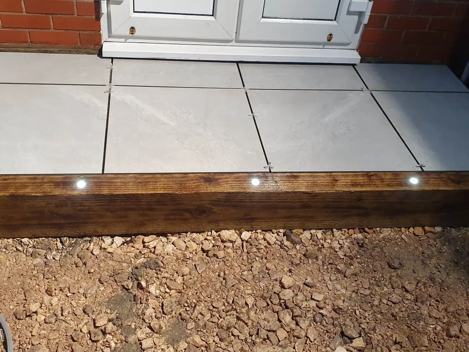 Grey porcelain patio edged with a sleeper and small deck lights