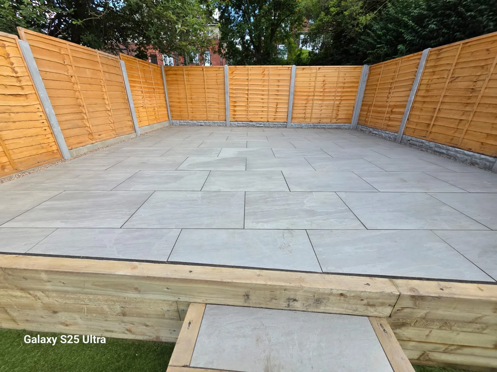 Grey porcelain patio with a sleeper edge and step in a fenced garden