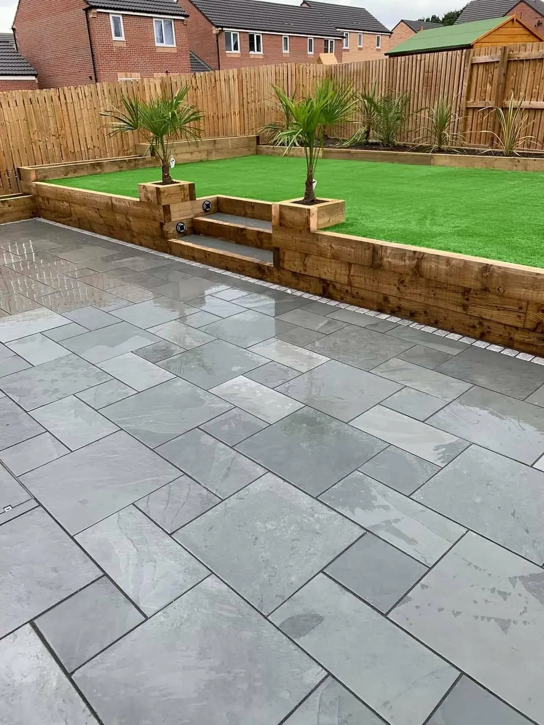Grey porcelain patio below a sleeper retaining wall with steps and palm planters
