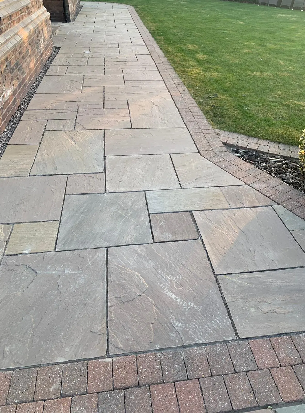 Grey sandstone path with red brick edging by a lawn