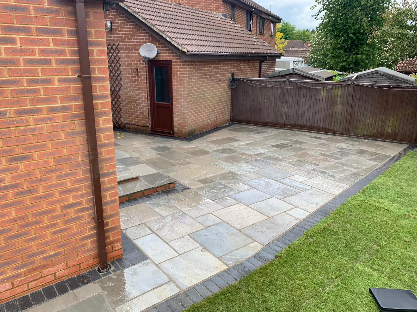 Grey sandstone patio with a charcoal border and a new lawn