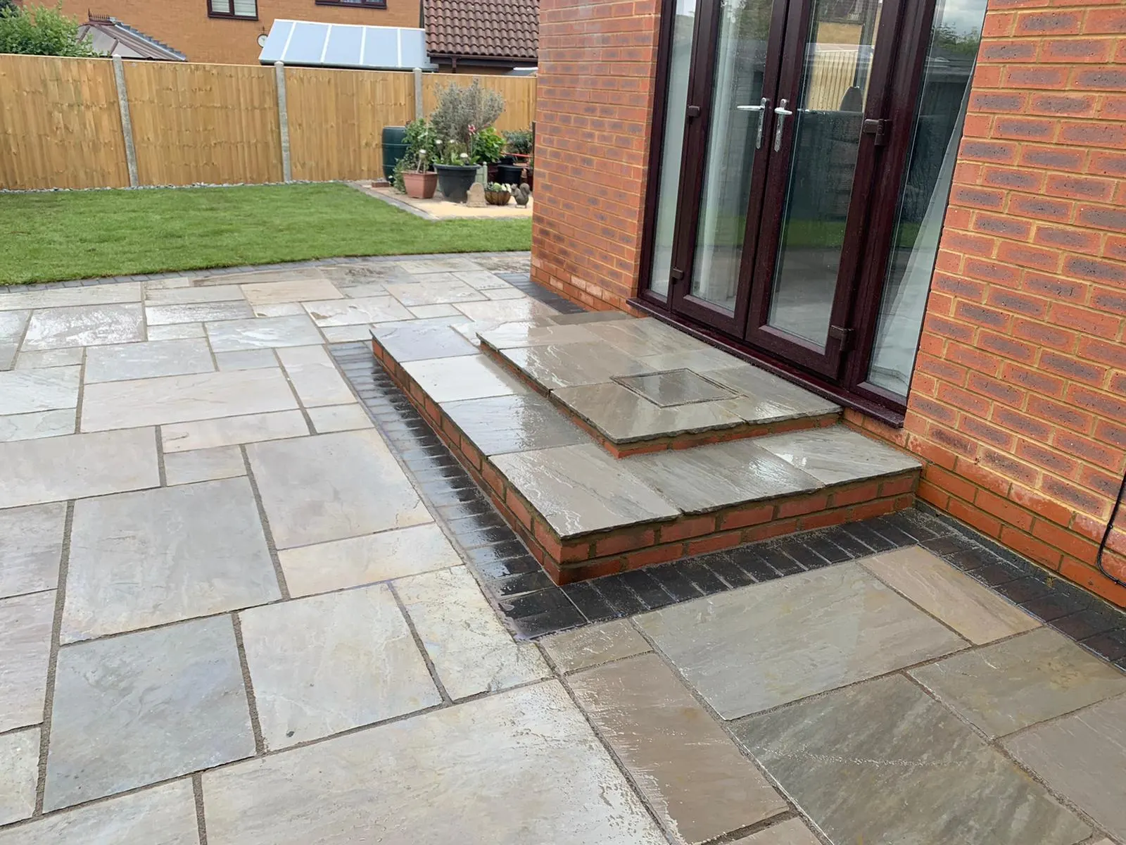 Grey sandstone patio with a step to French doors and a lawn