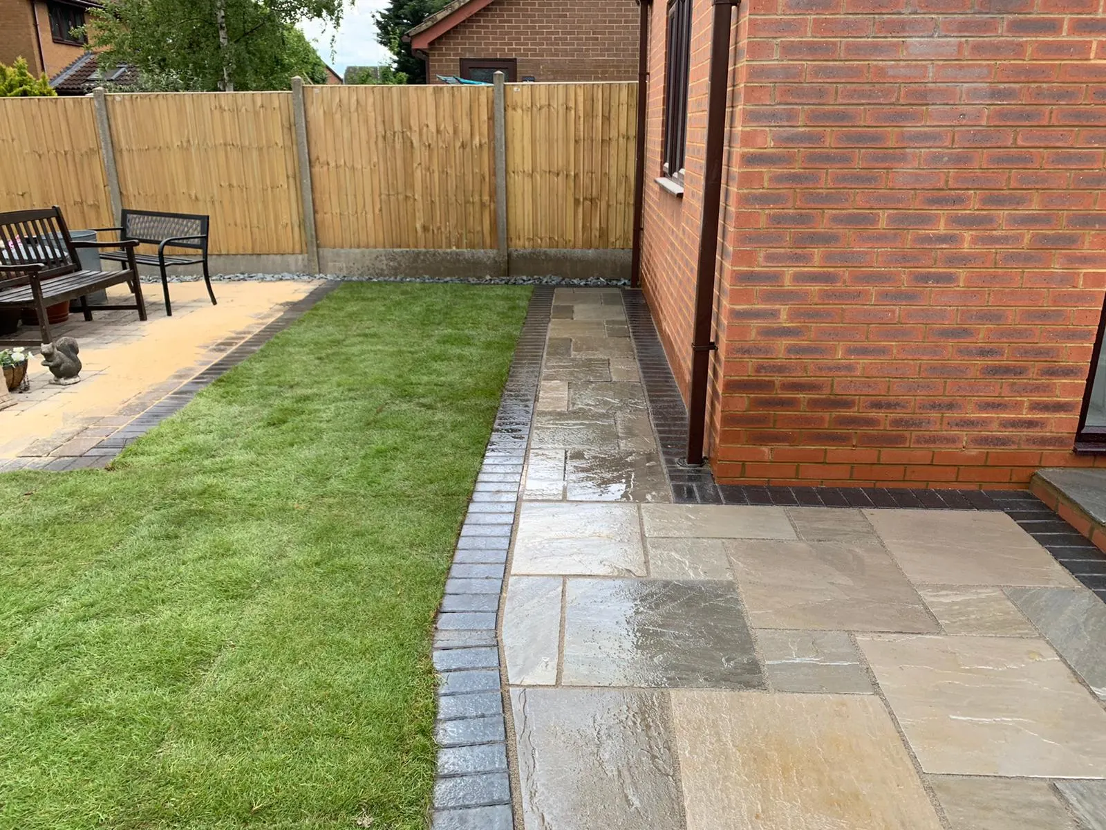 Grey sandstone patio with a charcoal edge beside a lawn at a bungalow
