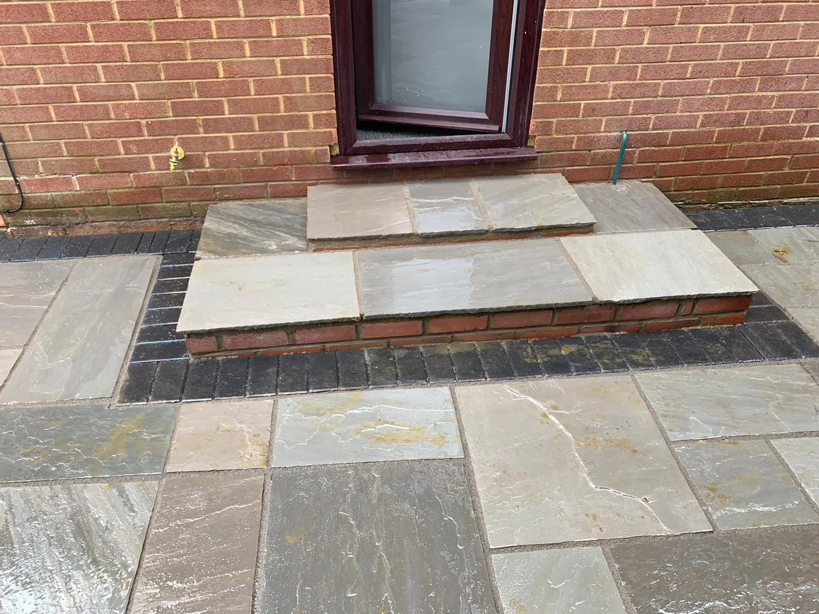 Grey sandstone patio with a raised step on a brick riser