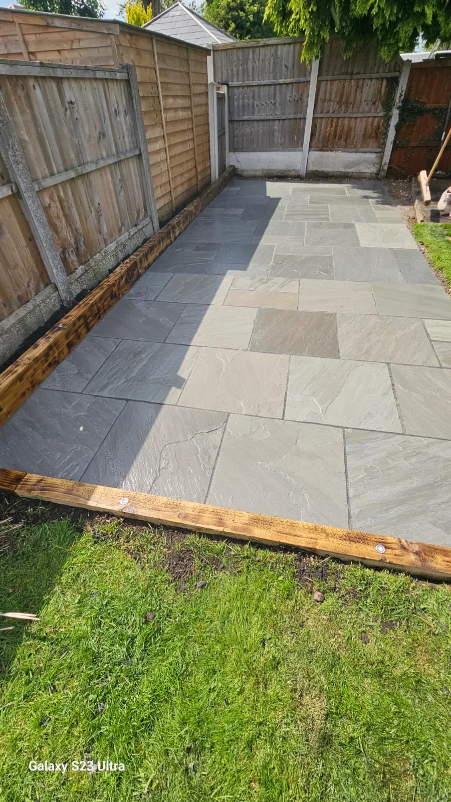 Grey sandstone patio with a sleeper edge above a lawn
