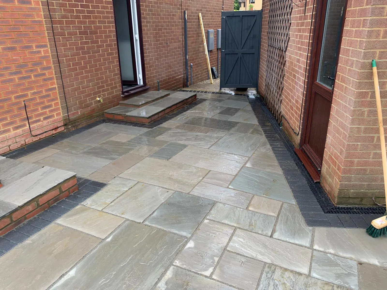 Grey sandstone patio with steps and a channel drain along the house