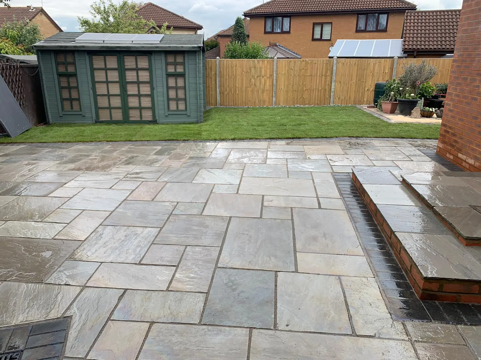 Grey sandstone patio with a step, a lawn and a summer house