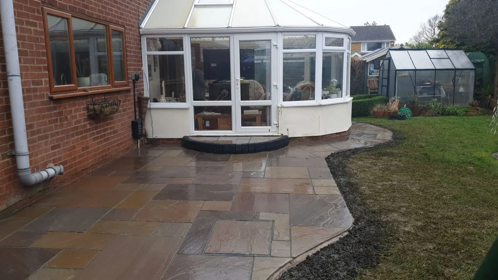 Indian sandstone patio curving round a conservatory and lawn