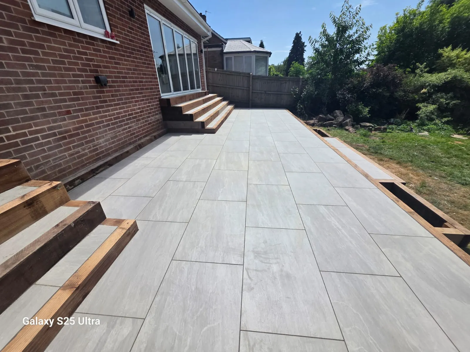 Large grey porcelain patio with sleeper steps beside a lawn