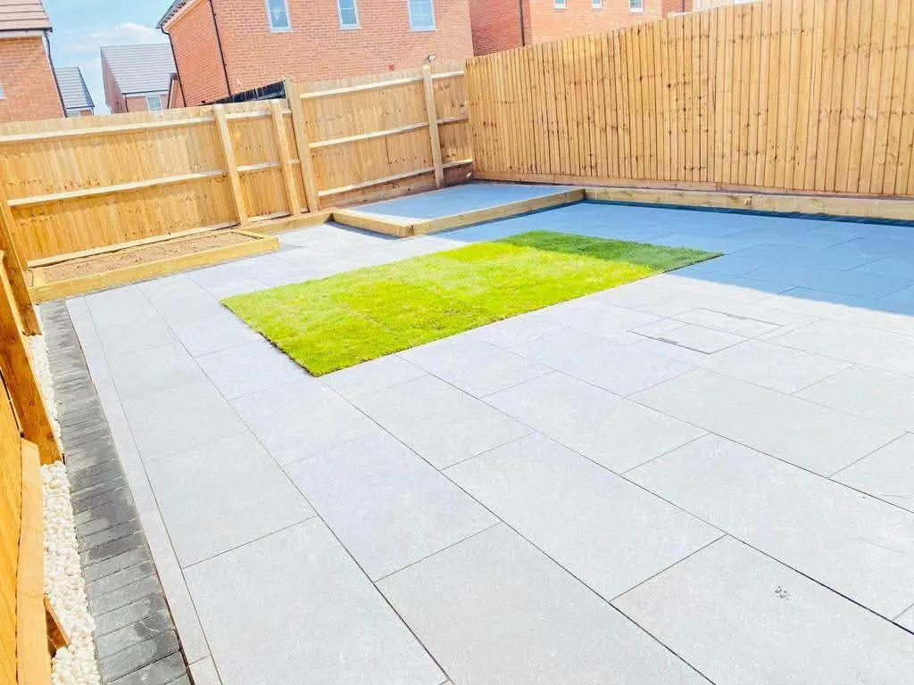 Light grey porcelain patio with an artificial grass inset in a fenced garden