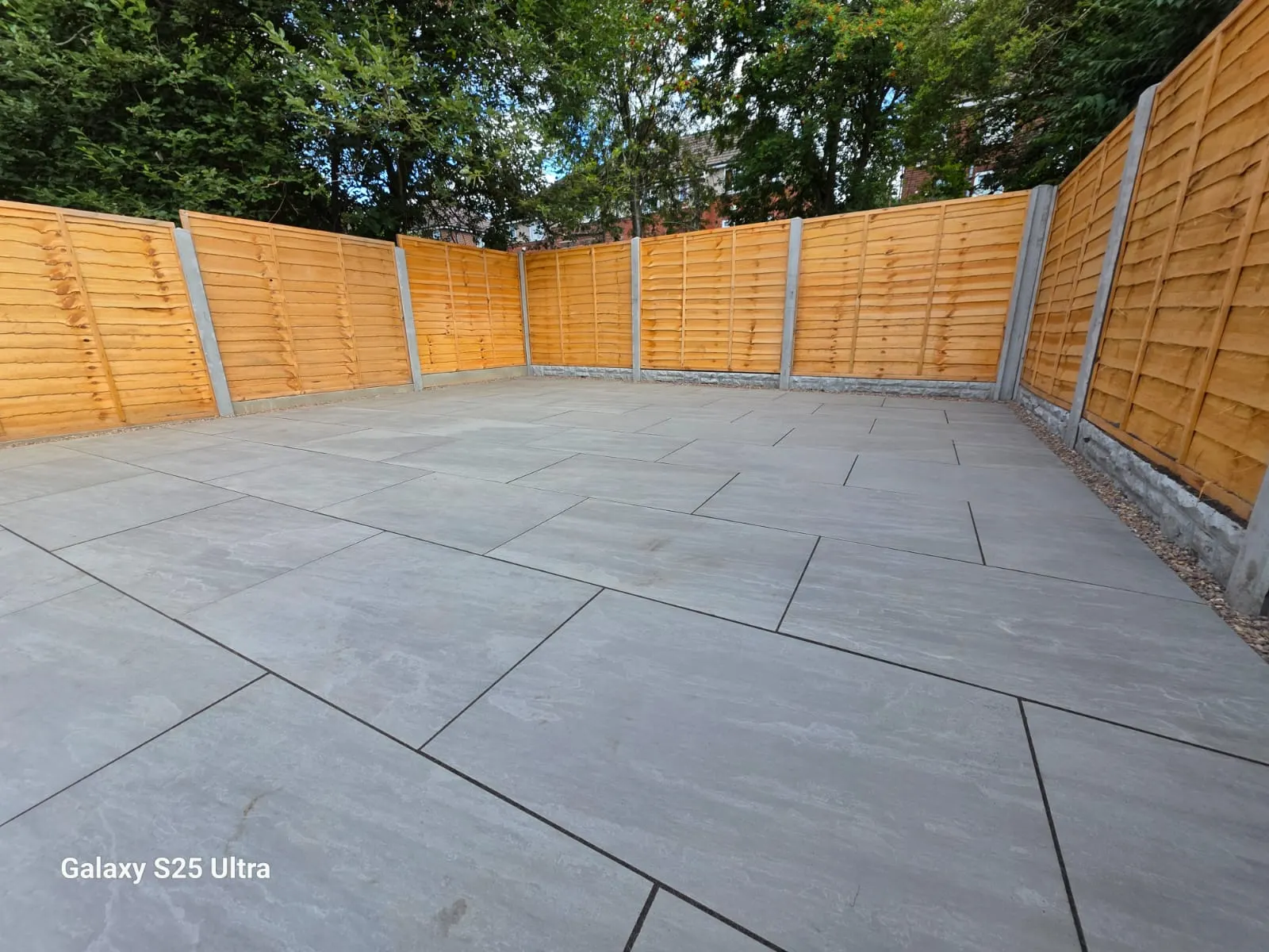 Light grey porcelain patio in the corner of a fenced garden